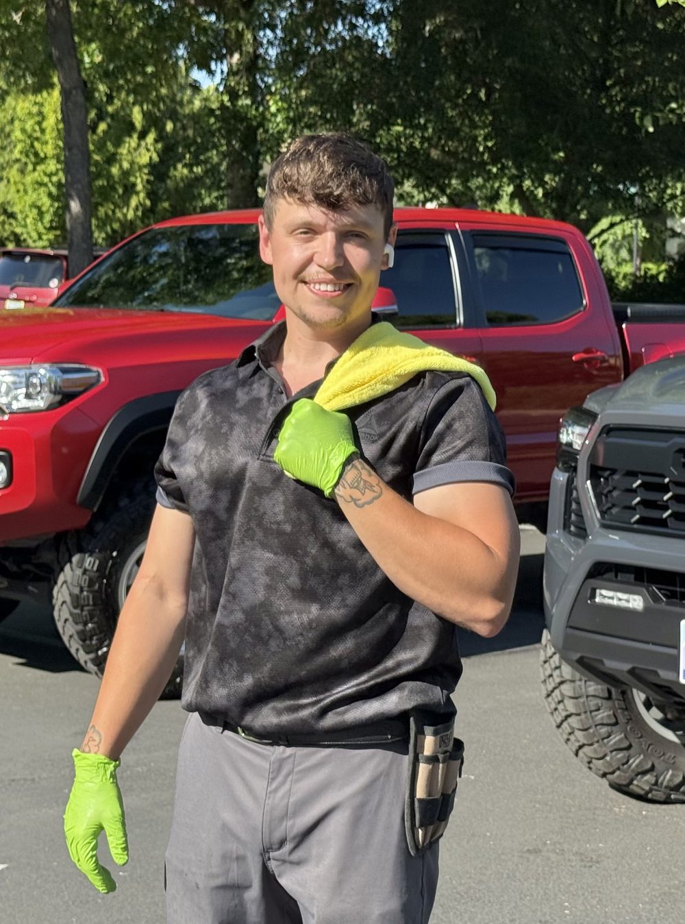 Kameron "Chuck" Taylor, USMC veteran and owner-operator of Xcalibur Mobile Detailing, in gloves with a drying towel beside two trucks